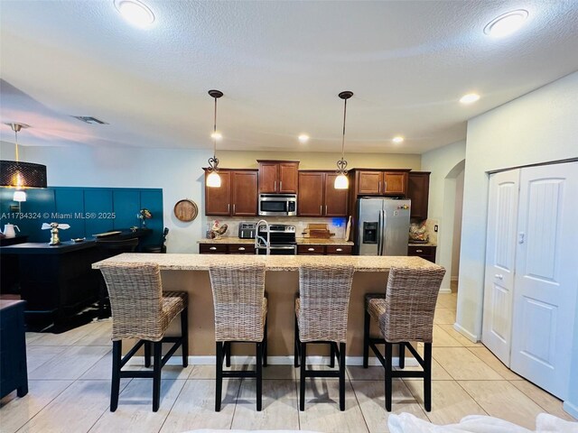 kitchen with stainless steel appliances, a kitchen island with sink, a kitchen bar, and decorative light fixtures