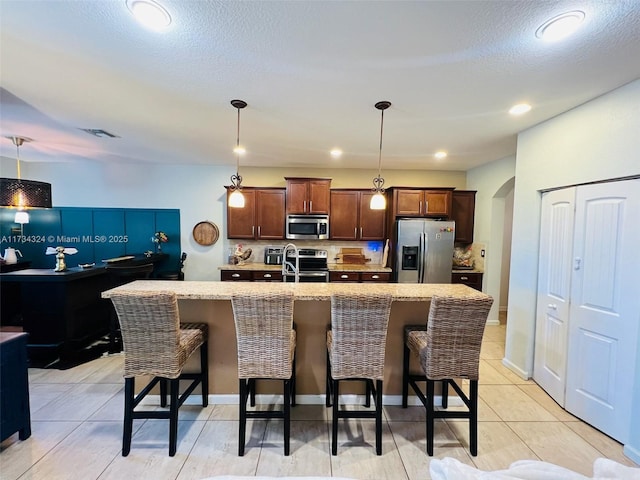 kitchen with stainless steel appliances, a kitchen island with sink, a kitchen bar, and decorative light fixtures