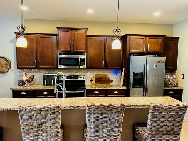 kitchen featuring pendant lighting, backsplash, light stone counters, and stainless steel appliances