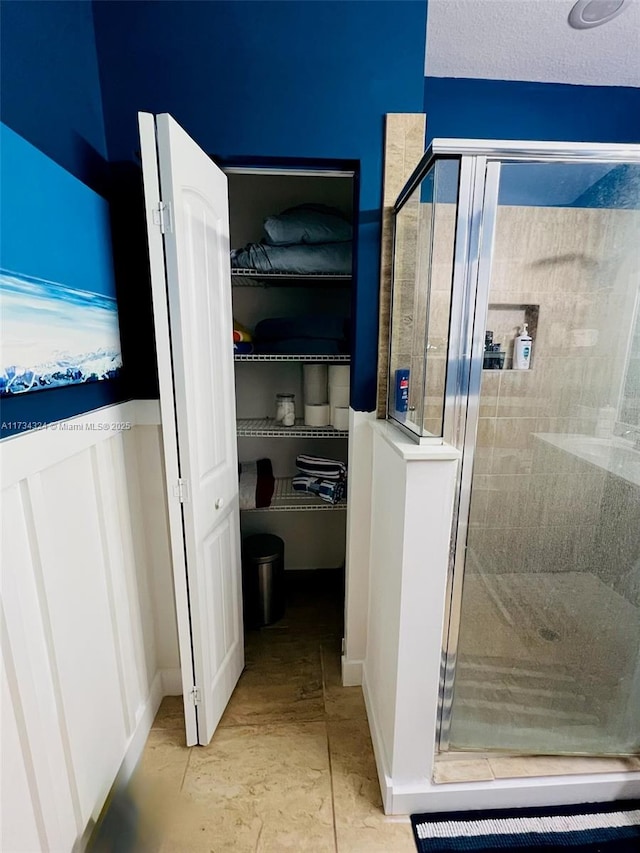 full bath featuring a walk in closet, a textured ceiling, and a stall shower