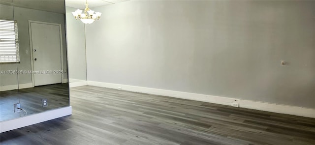 empty room featuring a notable chandelier, baseboards, and wood finished floors