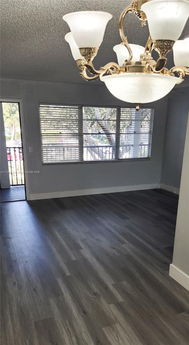 spare room featuring dark hardwood / wood-style flooring, a textured ceiling, and a notable chandelier