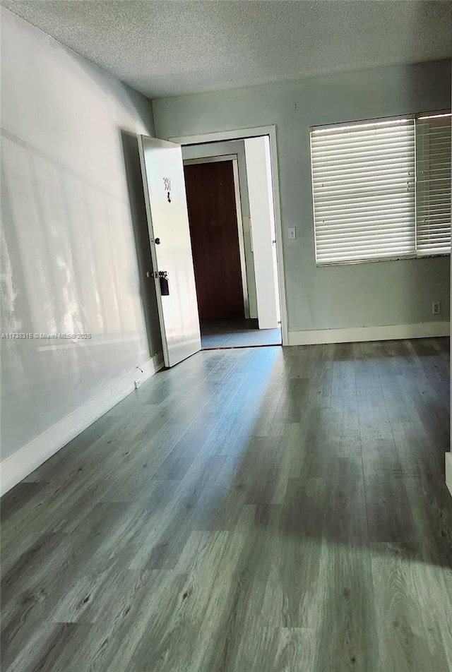 spare room featuring a textured ceiling, baseboards, and wood finished floors