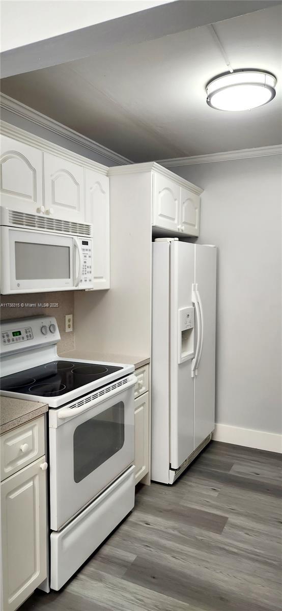 kitchen with hardwood / wood-style flooring, white cabinetry, ornamental molding, and white appliances