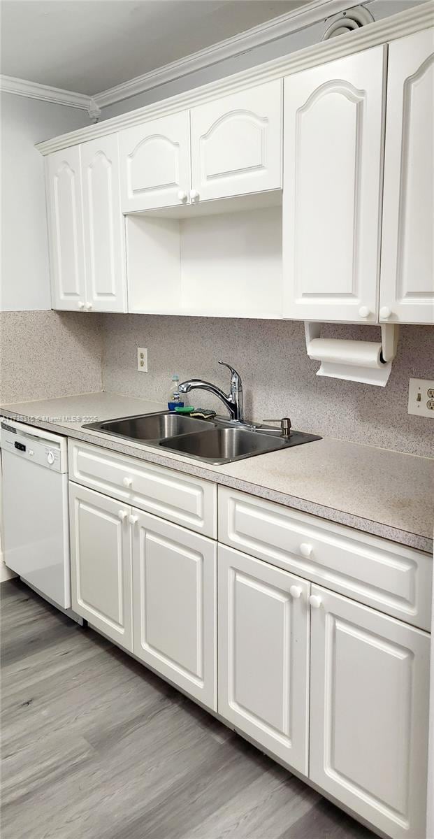 kitchen featuring white cabinets, white dishwasher, crown molding, light wood-style floors, and a sink