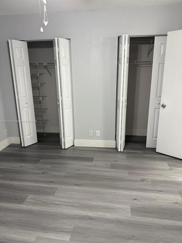 unfurnished bedroom featuring a textured ceiling, baseboards, multiple closets, and wood finished floors