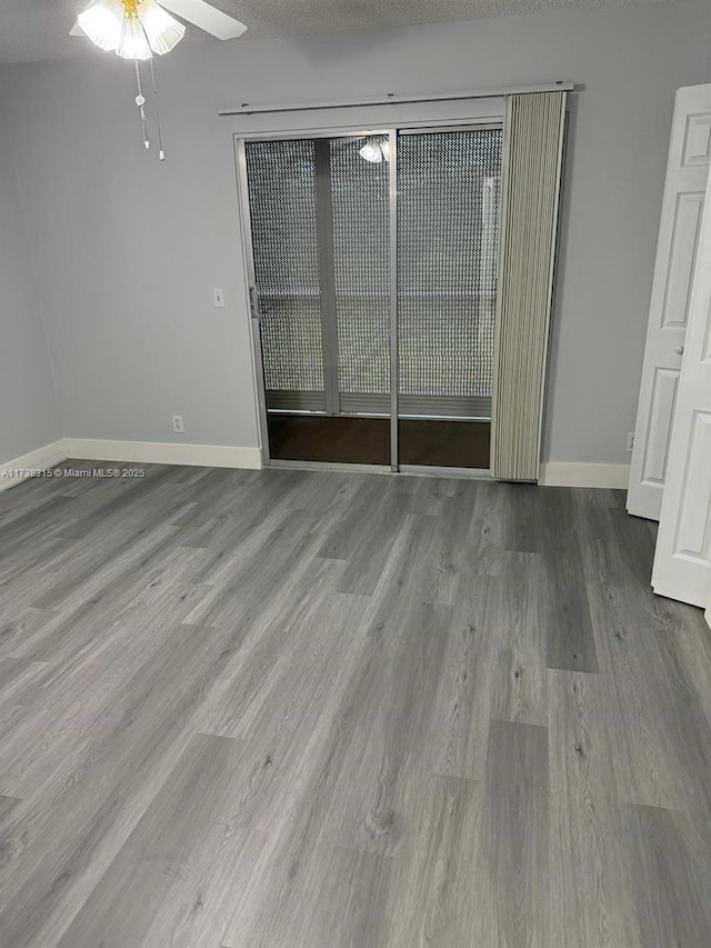 unfurnished room with a textured ceiling, wood finished floors, a ceiling fan, and baseboards