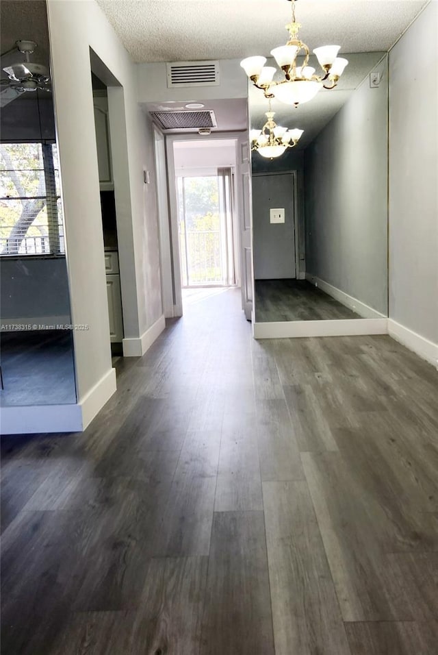 interior space with dark wood-style flooring, a notable chandelier, visible vents, a textured ceiling, and baseboards