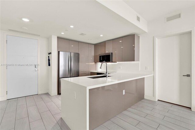 kitchen with gray cabinets, appliances with stainless steel finishes, sink, a breakfast bar area, and kitchen peninsula