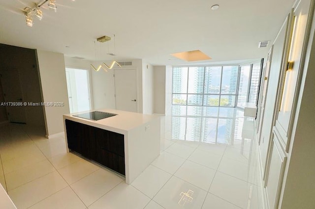 kitchen featuring pendant lighting, light tile patterned floors, a wall of windows, black electric stovetop, and a kitchen island