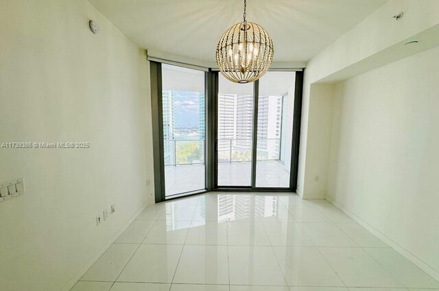 tiled spare room featuring floor to ceiling windows and a notable chandelier