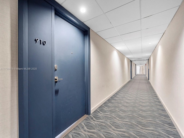 hallway featuring a drop ceiling and dark carpet