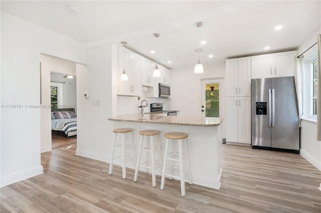 kitchen featuring light wood finished floors, stainless steel appliances, hanging light fixtures, white cabinetry, and a peninsula