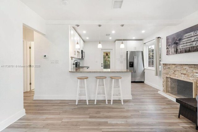 kitchen with white cabinetry, light stone counters, light wood-type flooring, kitchen peninsula, and stainless steel appliances