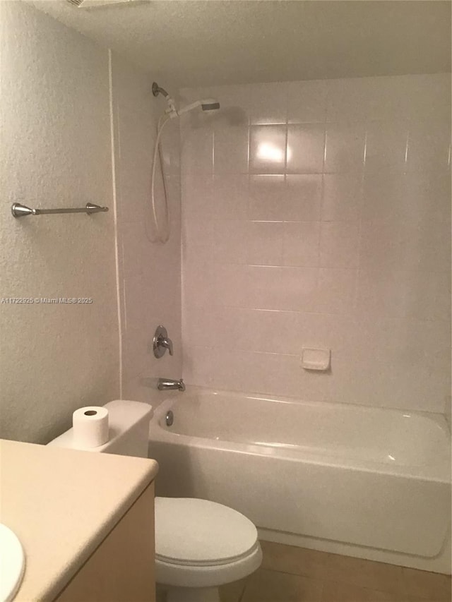 full bath featuring  shower combination, toilet, tile patterned flooring, a textured wall, and vanity