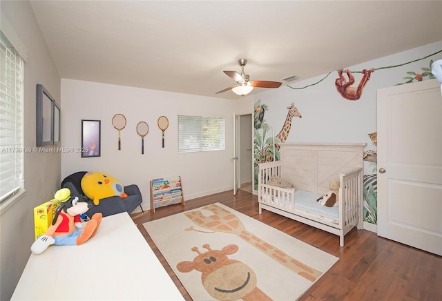 bedroom featuring dark wood-type flooring, ceiling fan, and a nursery area