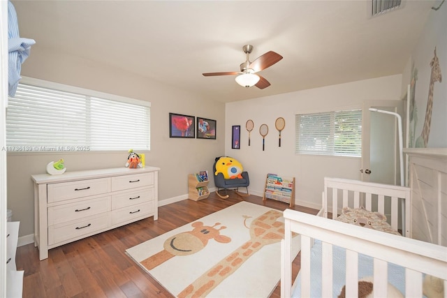 bedroom featuring a nursery area, ceiling fan, and dark hardwood / wood-style flooring