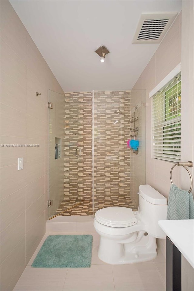 bathroom featuring a shower with door, tile walls, tile patterned flooring, vanity, and toilet