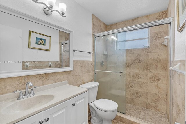 bathroom featuring tile walls, vanity, a shower with door, and toilet