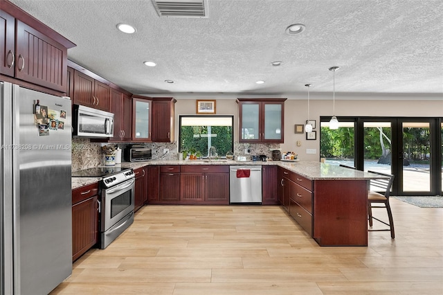 kitchen featuring pendant lighting, plenty of natural light, stainless steel appliances, light stone counters, and a kitchen bar