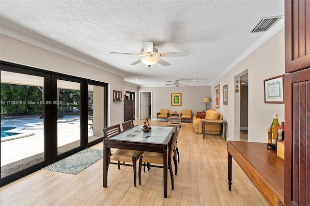 dining room featuring french doors, ornamental molding, a textured ceiling, and light wood-type flooring