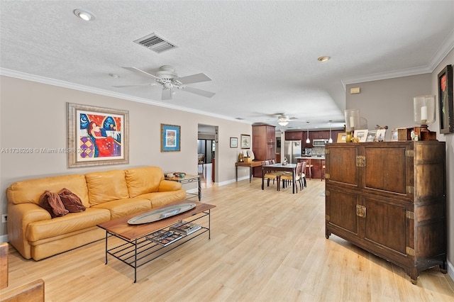 living room with ceiling fan, ornamental molding, light hardwood / wood-style floors, and a textured ceiling