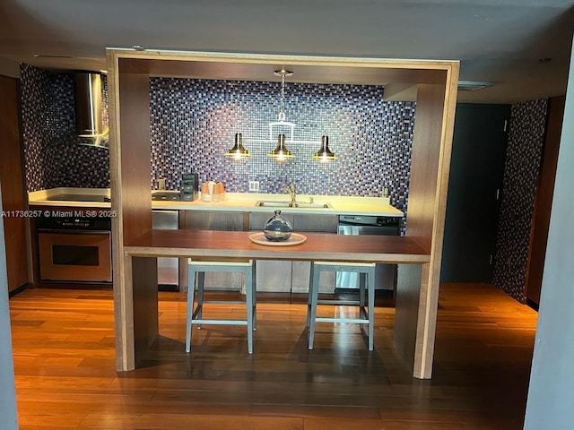 kitchen with decorative light fixtures, dishwasher, wood-type flooring, sink, and oven