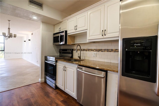 kitchen with stainless steel appliances, white cabinetry, sink, and dark stone countertops