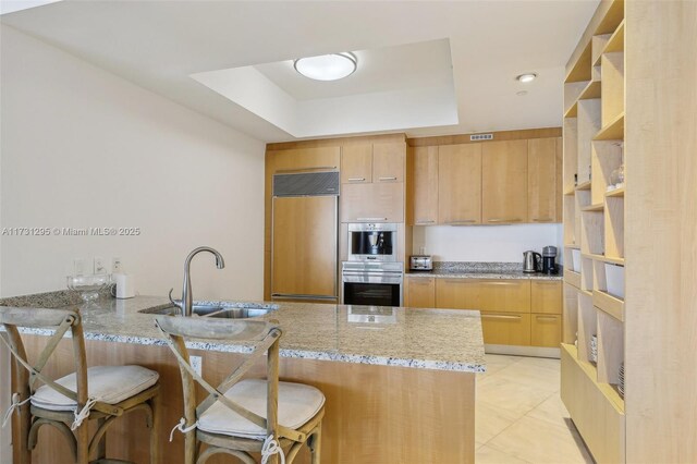 kitchen with open shelves, a sink, light stone countertops, paneled refrigerator, and a peninsula