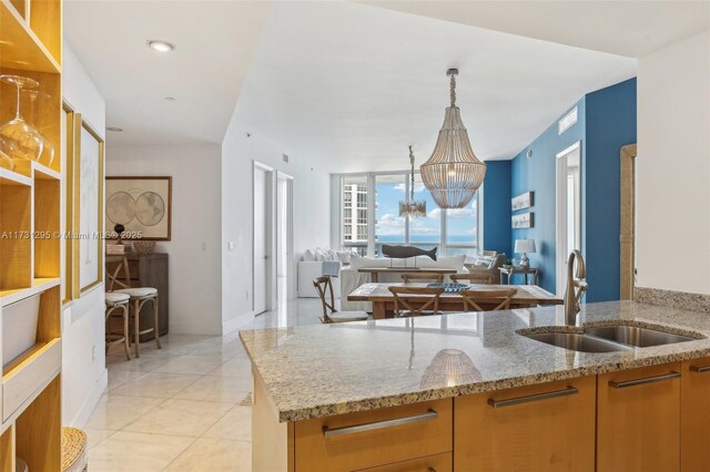 kitchen with a notable chandelier, light tile patterned floors, open floor plan, a sink, and light stone countertops