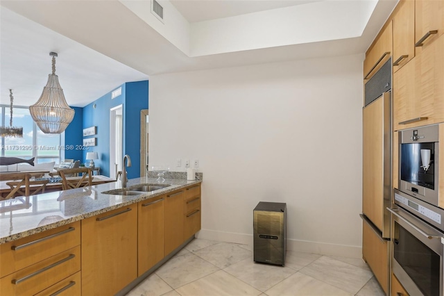 kitchen featuring oven, a sink, visible vents, light stone countertops, and decorative light fixtures