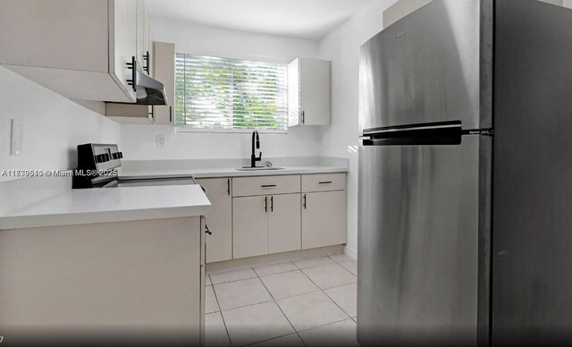 kitchen with stainless steel refrigerator, white cabinetry, sink, range, and light tile patterned floors