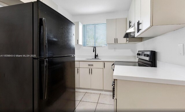 kitchen with light tile patterned flooring, black refrigerator, sink, and stainless steel electric stove