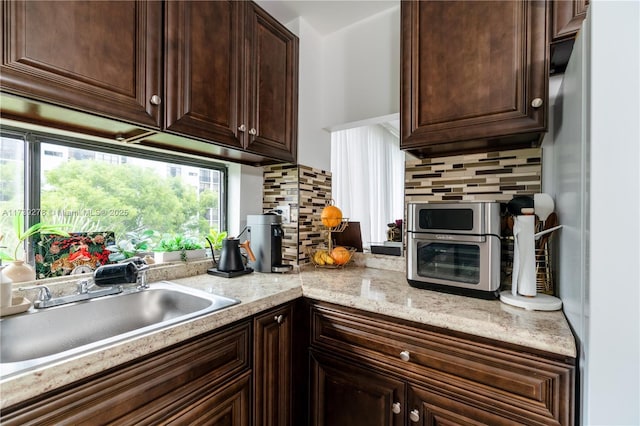 kitchen featuring sink, backsplash, white fridge, dark brown cabinetry, and light stone countertops