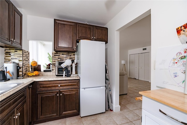 kitchen with backsplash, light tile patterned floors, dark brown cabinets, and white fridge