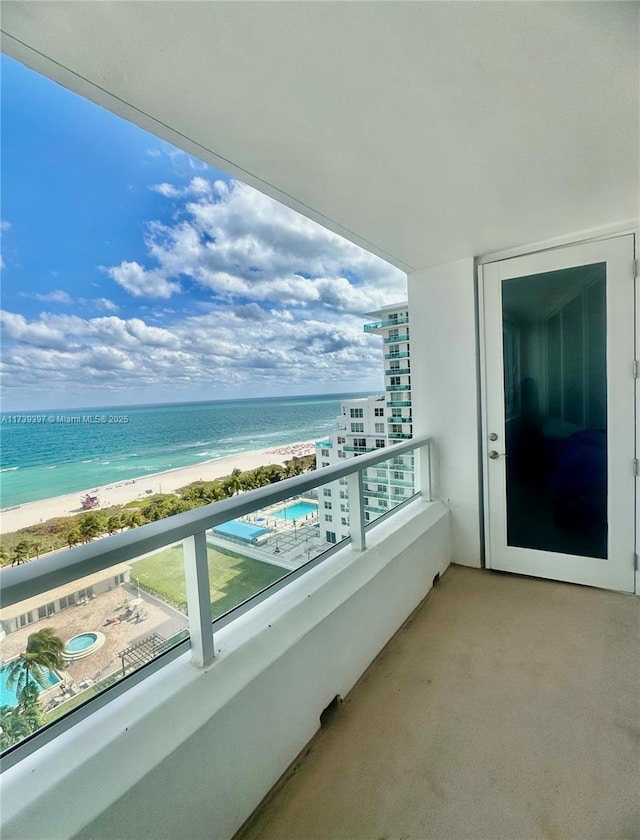 balcony featuring a water view, a hot tub, and a beach view