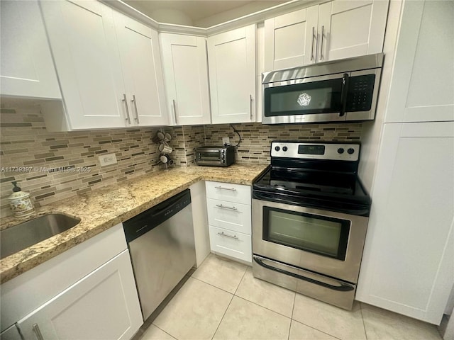 kitchen featuring light tile patterned floors, light stone counters, stainless steel appliances, white cabinetry, and backsplash