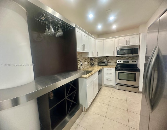 kitchen featuring stainless steel appliances, a sink, white cabinetry, backsplash, and light stone countertops