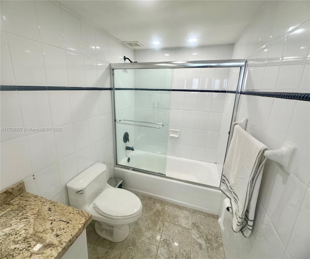 full bathroom featuring toilet, bath / shower combo with glass door, visible vents, vanity, and tile walls