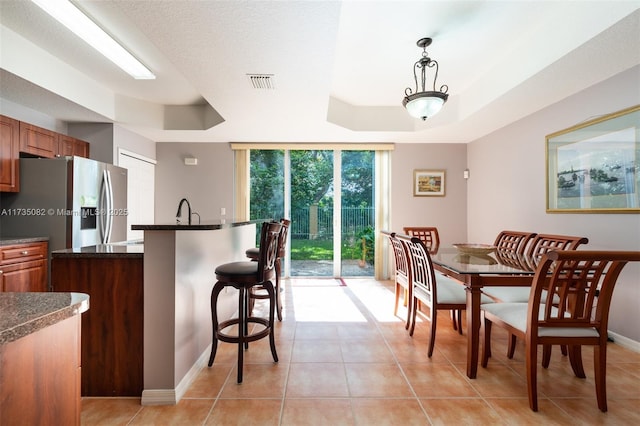 kitchen featuring light tile patterned flooring, a breakfast bar area, decorative light fixtures, a raised ceiling, and expansive windows