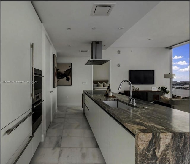 kitchen with island range hood, sink, white cabinets, dark stone counters, and black electric cooktop