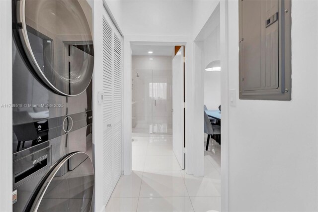 clothes washing area featuring stacked washer and dryer, light tile patterned floors, and electric panel