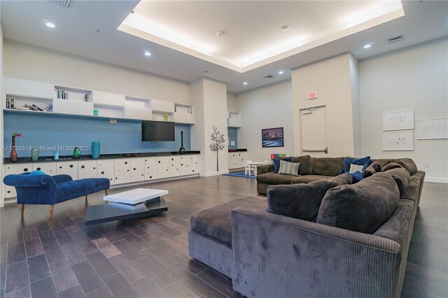 living room featuring a high ceiling, dark wood-type flooring, and a tray ceiling