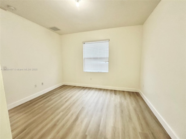 spare room with baseboards, visible vents, and wood finished floors