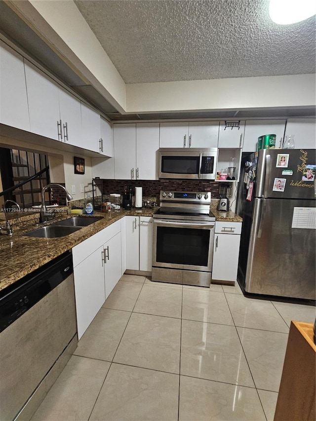 kitchen featuring sink, stainless steel appliances, white cabinets, light tile patterned flooring, and dark stone counters