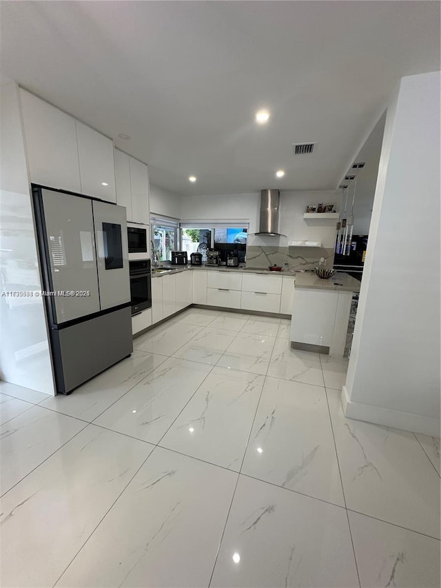 kitchen featuring black oven, wall chimney exhaust hood, white cabinets, and refrigerator