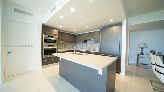 kitchen with sink, a center island with sink, black electric cooktop, decorative backsplash, and stainless steel double oven