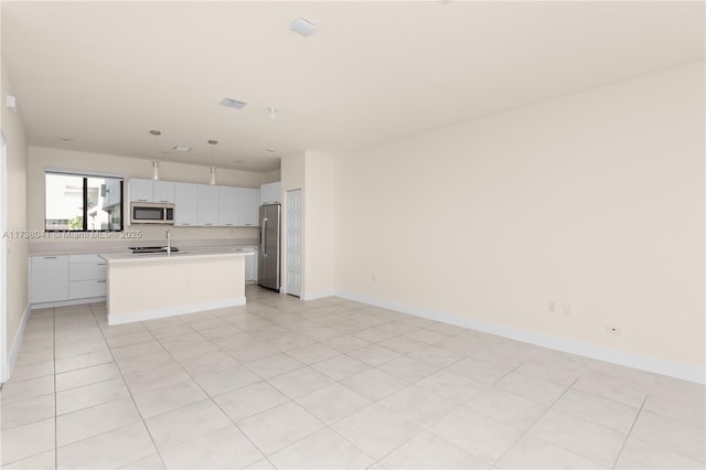 kitchen with stainless steel appliances, light tile patterned floors, sink, white cabinetry, and a kitchen island with sink