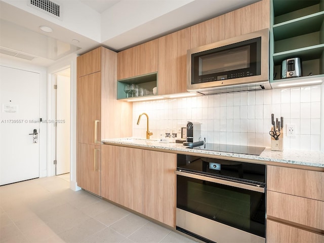 kitchen with wall oven, light stone countertops, black electric cooktop, and light brown cabinets