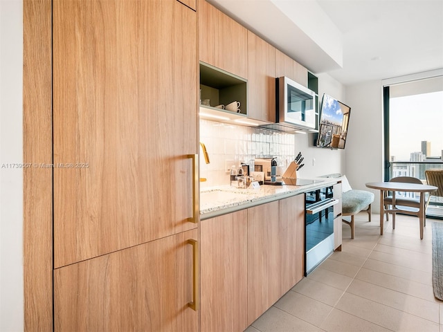 kitchen with light tile patterned floors, light brown cabinets, stainless steel appliances, light stone countertops, and decorative backsplash